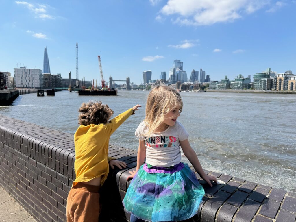 a boy and girl standing on a brick wall by water and a city