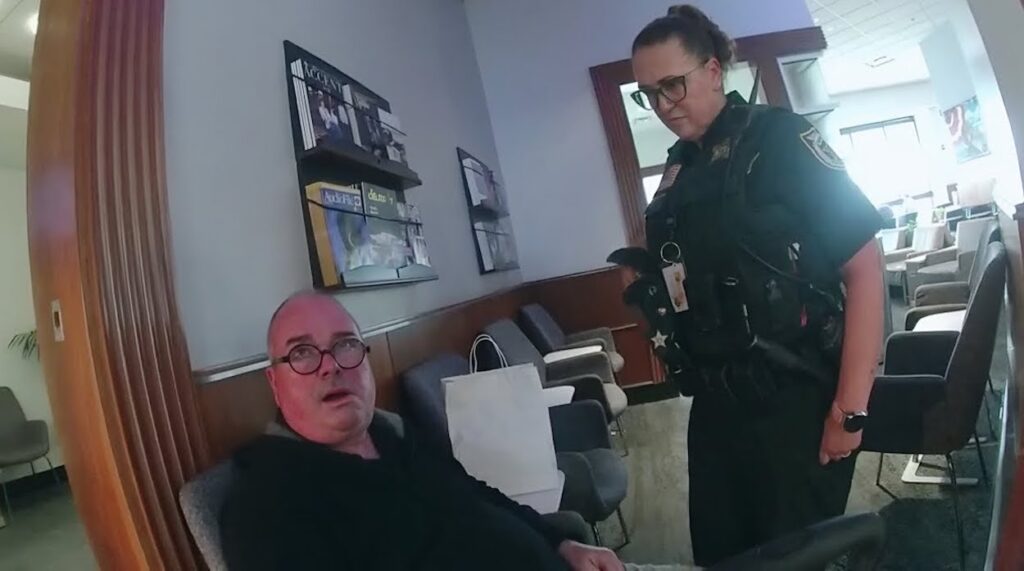 a man sitting on a couch with a police officer standing next to him