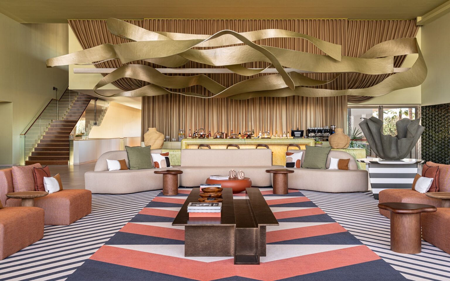kimpton algarve lobby with orange and brown patterned carpet below gold sculptural ceiling installation