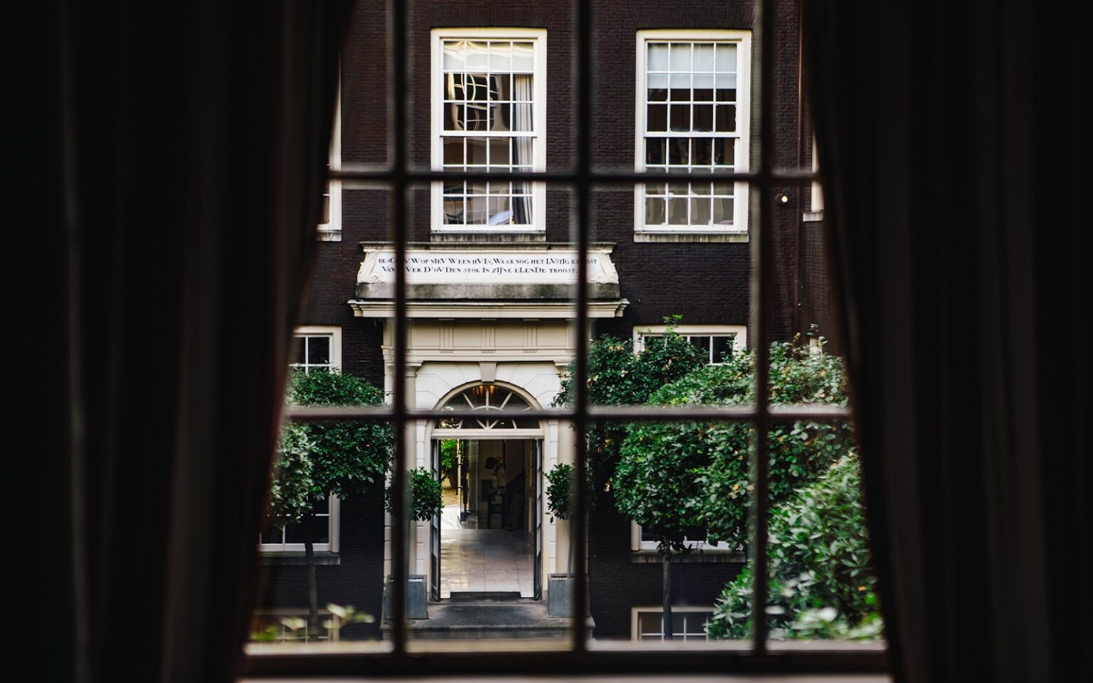 The Dylan Amsterdam – a canal-side reinvention view of hotel entrance through curtains and window at The dylan amsterdam