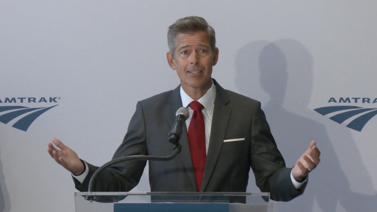 a man in a suit and tie standing at a podium with his hands up