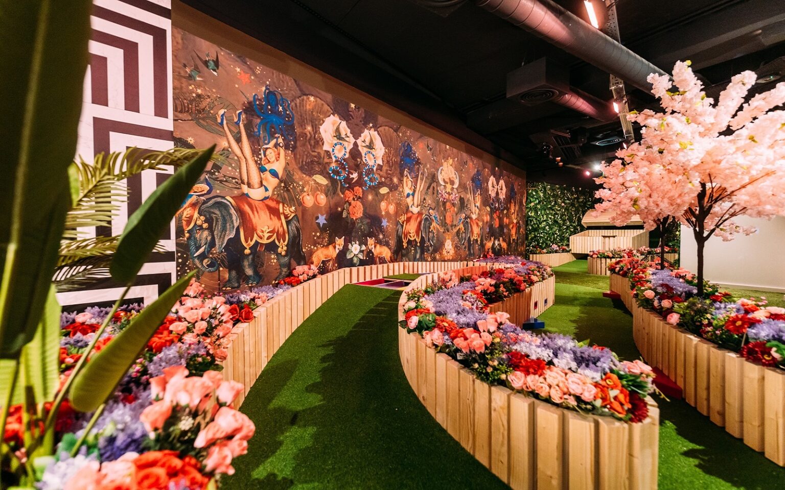 Newmor harnesses the power of play entrance ramp to game venue with a green path lined with fake flowers and bright patterned wall coverings from Newmor