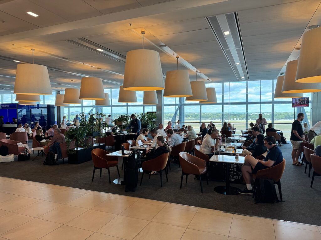 Review: British Airways Club Lounge North – London (LHR – T5) a group of people sitting at tables in a room with large windows