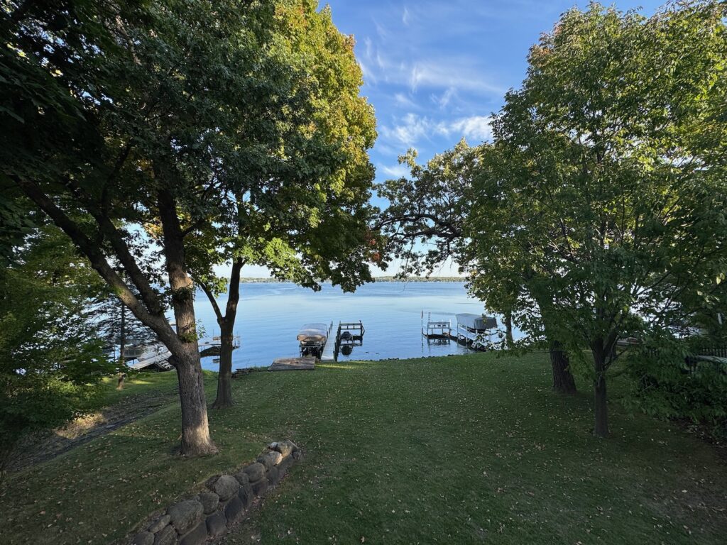Returning To Green Lake, Wisconsin: 14 Years Of Friendship And Tradition a grass lawn with trees and a dock on the water