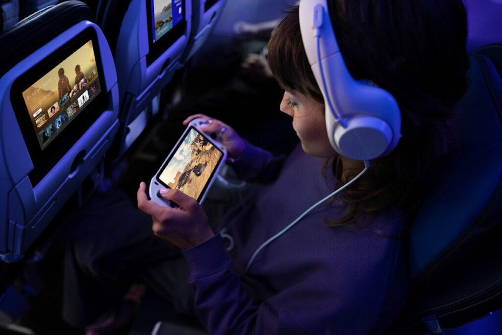 United Airlines Debuts Free Starlink Wi-Fi On First Mainline Aircraft Passenger enjoying in-flight entertainment on a smartphone while wearing headphones, with personal screen displaying streaming options, highlighting United Airlines