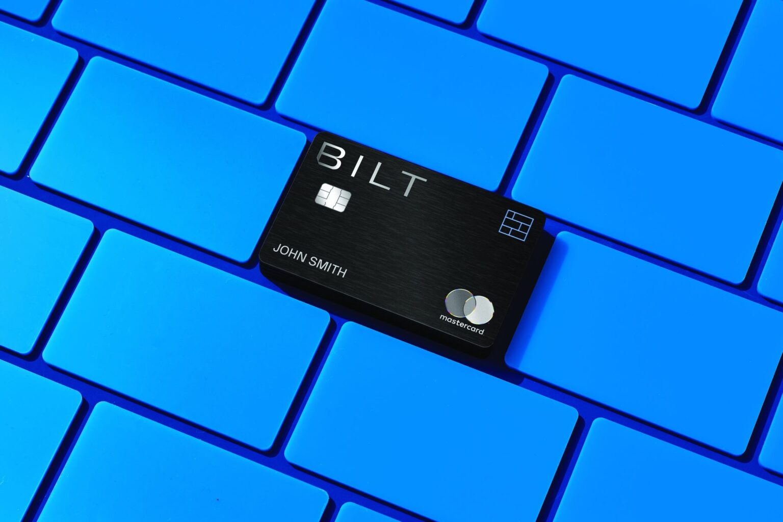 Bilt Mastercard on blue keyboard, highlighting Rent Day benefits for earning points on dining and travel.