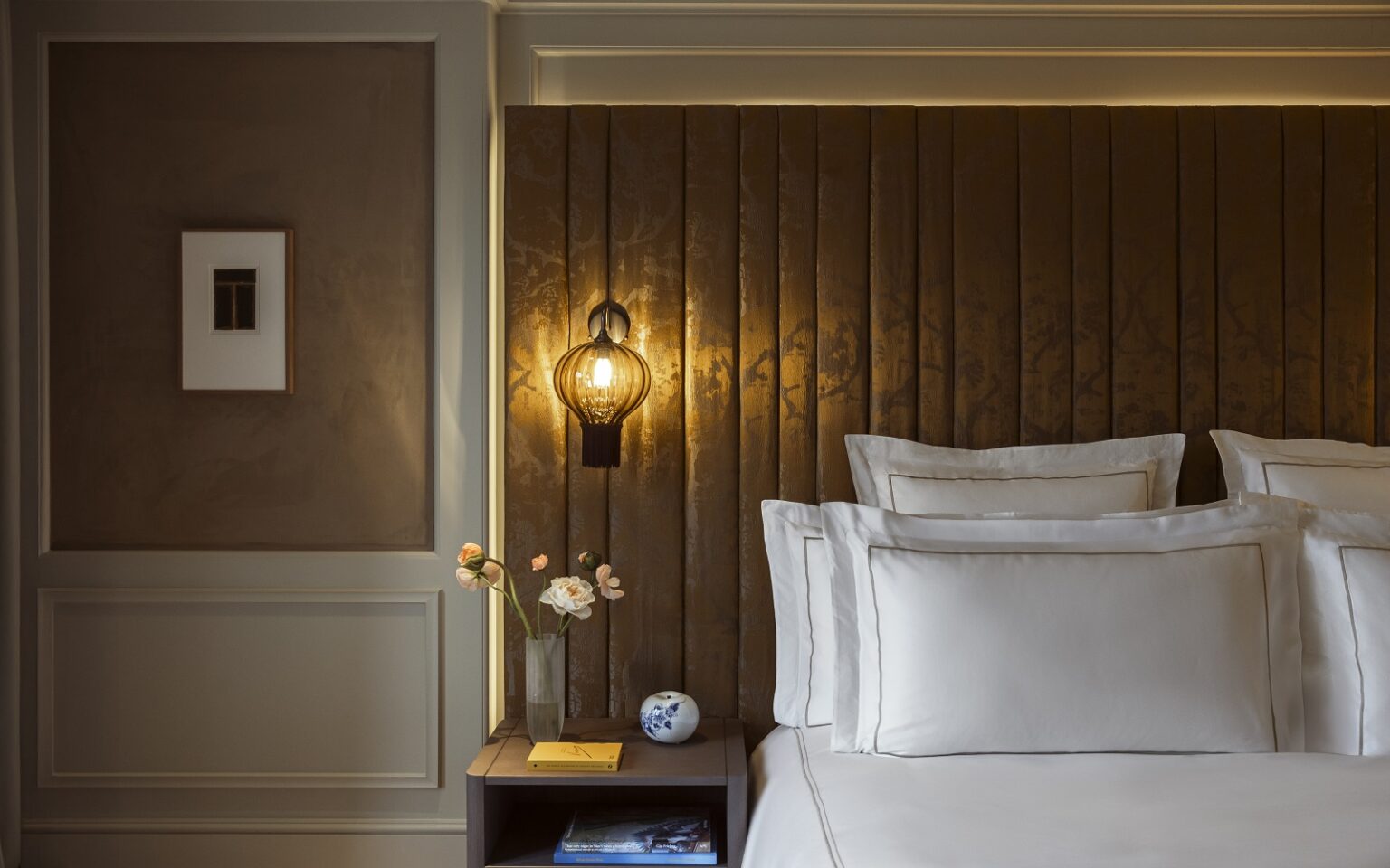 detail of bed with white linen against panelled headboard and suspended bedside light in Rosewood Amsterdam guestroom