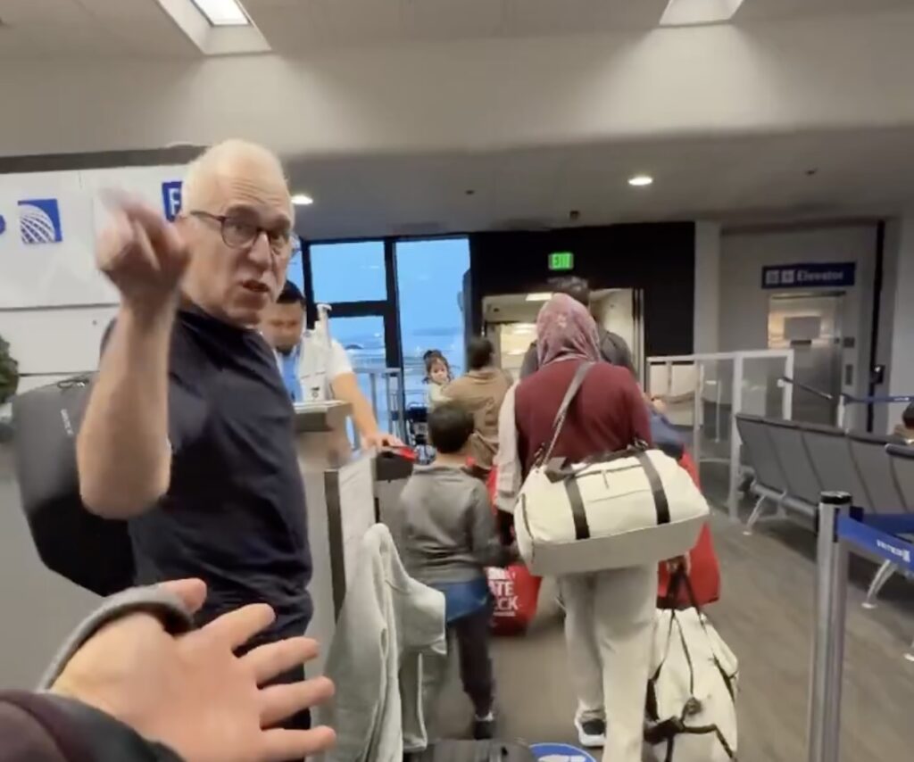 United Global Services Member Throws Fit After Family Boards Before Him a man standing in a room with luggage