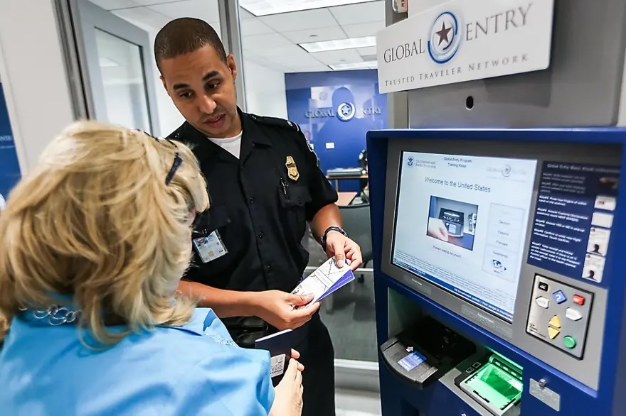 Trump Administration Reopened TSA PreCheck — So Why Is Global Entry Still Shut Down? a man in uniform and a woman in front of a machine