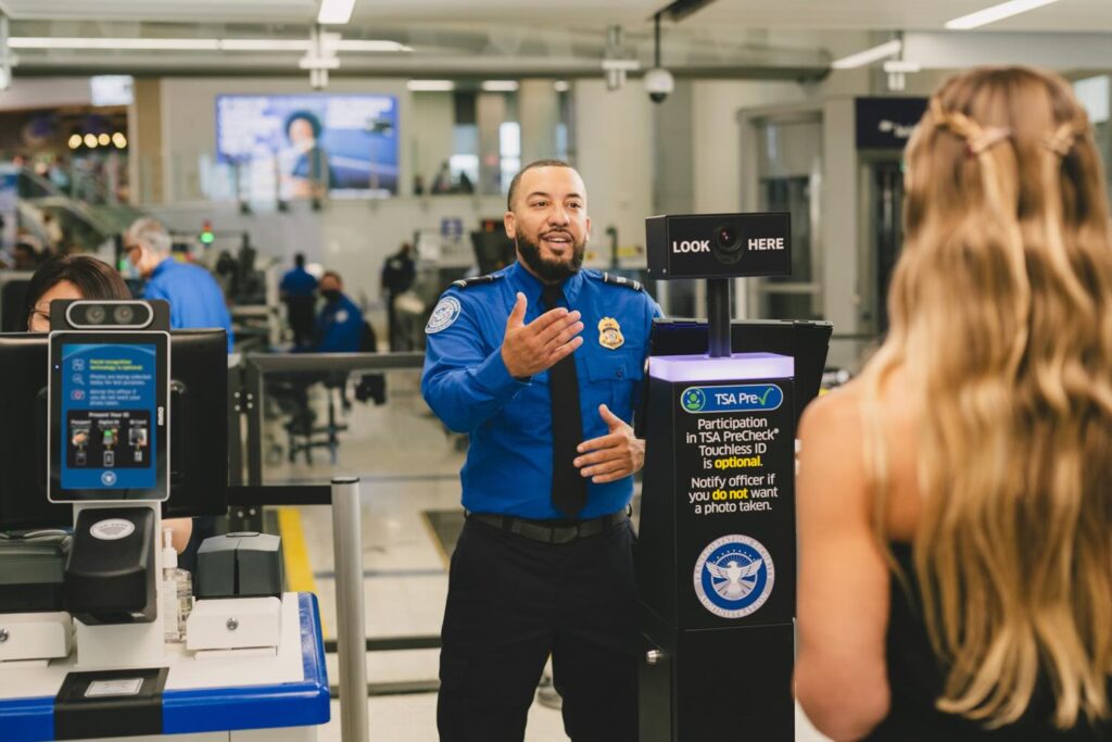 Timeline Of Incompetence: Trump DHS Reinstates TSA PreCheck Hours After Shutting It Down a man in a blue shirt talking to a woman