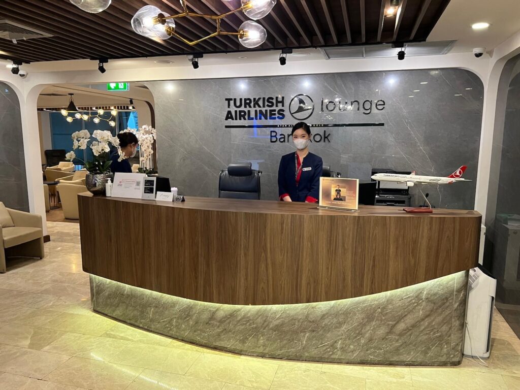 Turkish Airlines Lounge Bangkok reception area with staff member in uniform, modern decor, and floral arrangements.