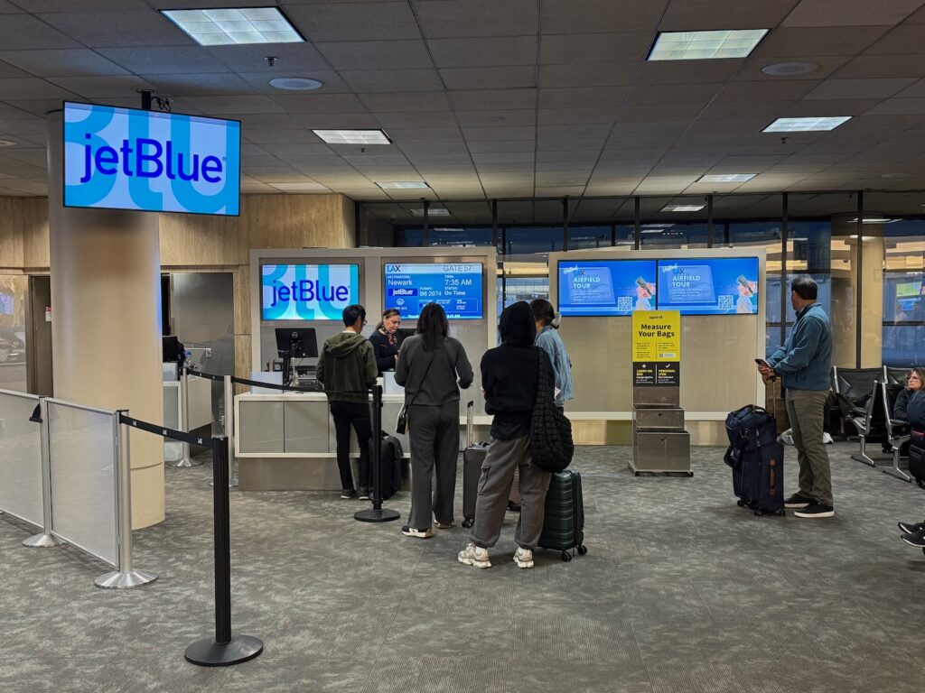 JetBlue Says It Is Raising Bag Fees Again To Keep Fares “Low” And Wi-Fi Free people standing in front of a computer