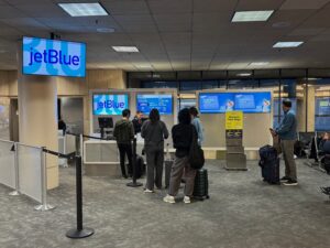 JetBlue Says It Is Raising Bag Fees Again To Keep Fares “Low” And Wi-Fi Free people standing in front of a computer