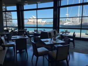 Hyatt Needs To Crack Down On The Park Hyatt Sydney… a room with tables and chairs and a large window with a boat in the background