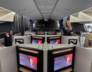 American Airlines Wants To Be A “Premier Global Airline,” But I’d Settle For A Working Seat And An On-Time Flight a woman standing in a room with several monitors